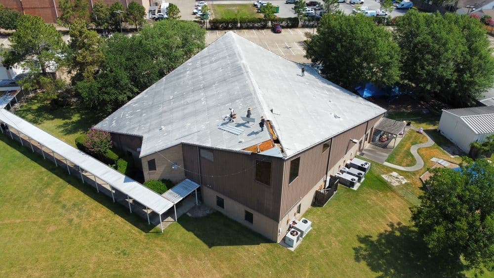 Aerial view of a large building with workers on the roof, surrounded by green space.
