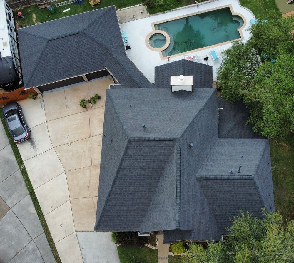 Aerial view of a modern home with a black roof and pool in the backyard.