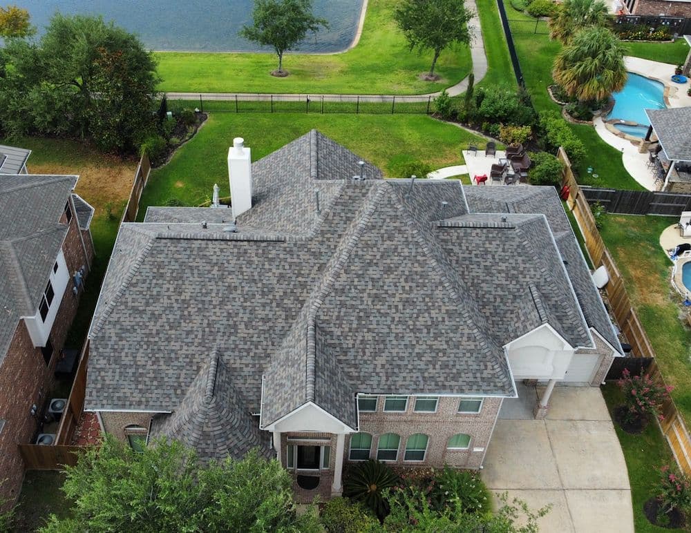 Aerial view of a stylish home with a grey shingle roof and landscaped yard.