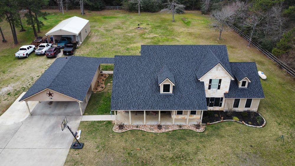 Aerial view of a modern house with a spacious yard and carport surrounded by trees.